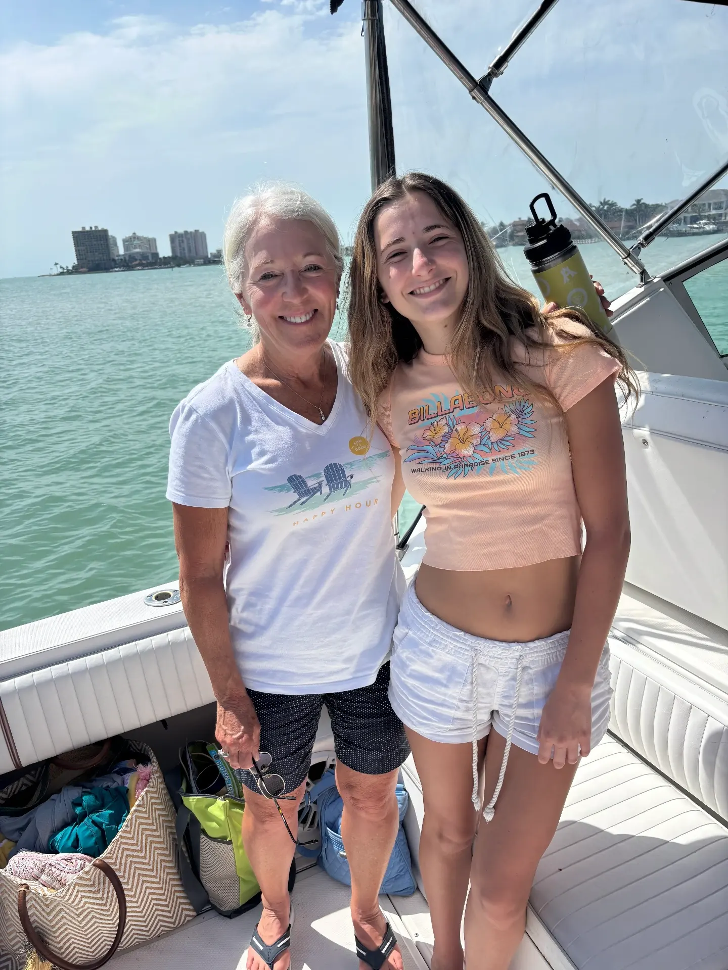 Two guests, one older and one younger, standing arm in arm on the aft deck with the shoreline behind them