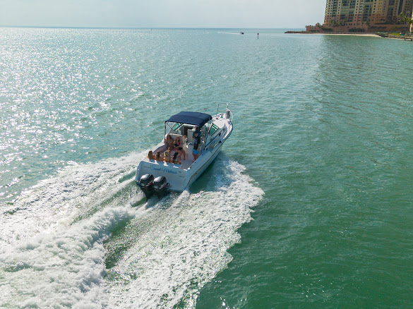 The Sweet Melissa under way past the rock jetty below the Cape Marco tower, a wake spreading behind her