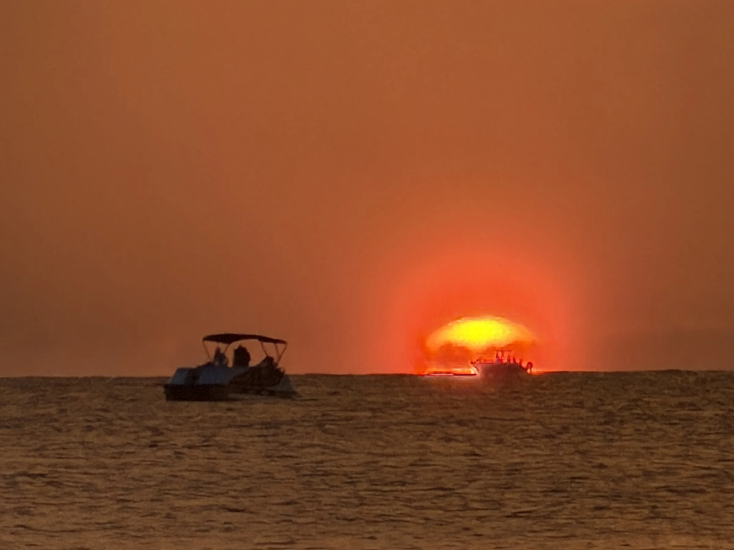 Two boats on a flat horizon as the sun drops into the Gulf off Marco Island