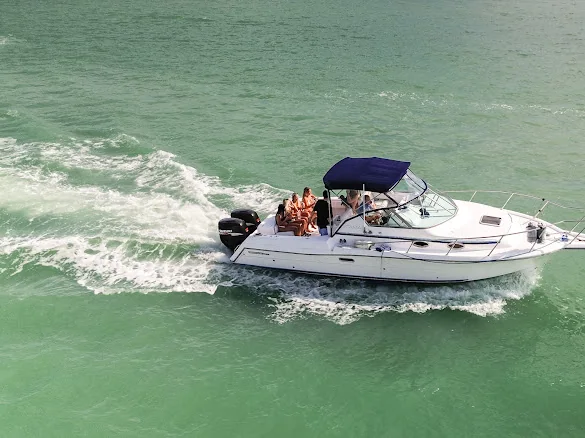 The Sweet Melissa seen from above, running across pale green water with her wake curving out behind her and a few guests small on the deck